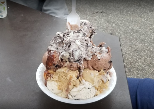 A large bowl of ice cream with multiple flavors, topped with whipped cream and a plastic spoon.
