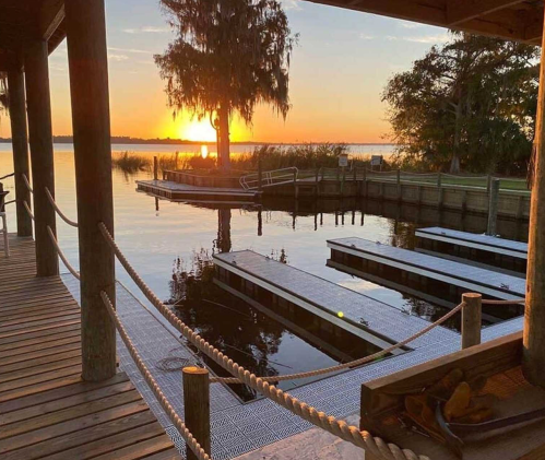 Sunset over a calm lake, with docks and trees silhouetted against the colorful sky.