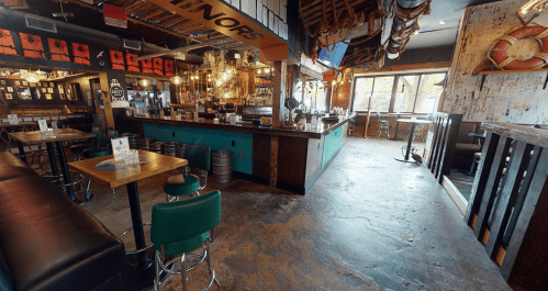 A vibrant bar interior featuring a wooden counter, green stools, and nautical decor, with large windows and a cozy atmosphere.