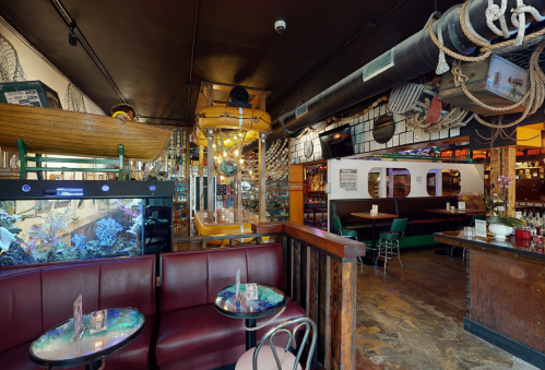 A vibrant restaurant interior featuring a boat decor, fish tank, and cozy seating areas with colorful lighting.
