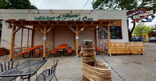 Outdoor seating area of a restaurant with wooden tables and a covered patio, surrounded by trees and a nautical theme.