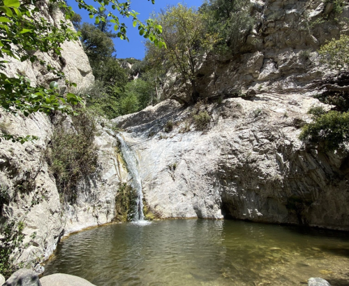 A serene natural scene featuring a small waterfall cascading into a clear pool surrounded by rocky cliffs and greenery.