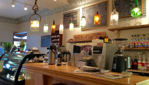 Cozy café interior with a wooden counter, colorful pendant lights, a coffee machine, and a display of pastries.