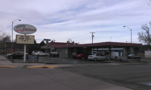 A restaurant sign for "Lippis Kitchen" with a parking lot and several cars, under a cloudy sky. Open daily 7 to 3.