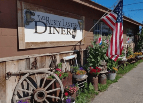 A rustic diner sign with an American flag, surrounded by colorful flowers and vintage decor.