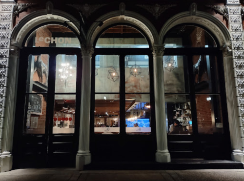 A nighttime view of a restaurant's arched entrance with large glass doors and decorative architectural details.
