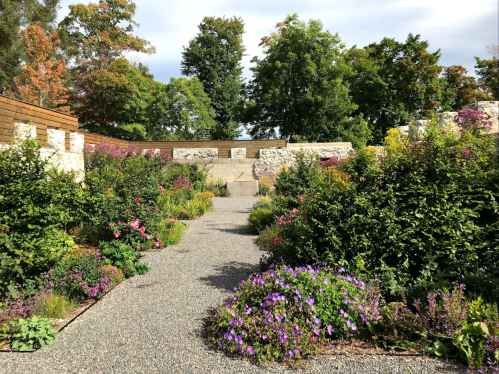 A scenic garden path surrounded by colorful flowers and lush greenery, with stone walls in the background.