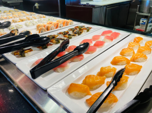 A sushi display featuring various types of sushi and sashimi on white plates with tongs for serving.