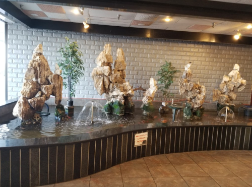 Indoor water feature with rock formations and small fountains, surrounded by potted plants and tiled flooring.