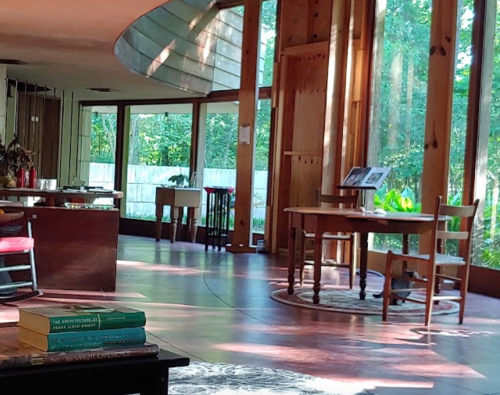 A bright, modern interior with large windows, wooden furniture, and a view of greenery outside.