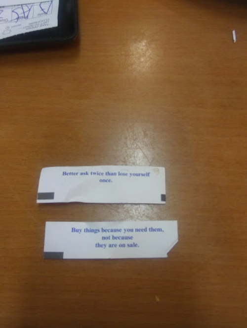 Two paper strips with motivational quotes on a wooden table. One advises to ask twice; the other on mindful shopping.