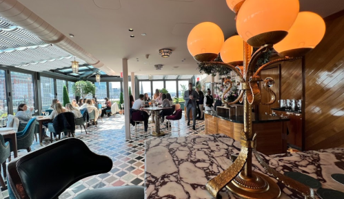 A stylish restaurant interior with large windows, elegant decor, and diners enjoying their meals at various tables.
