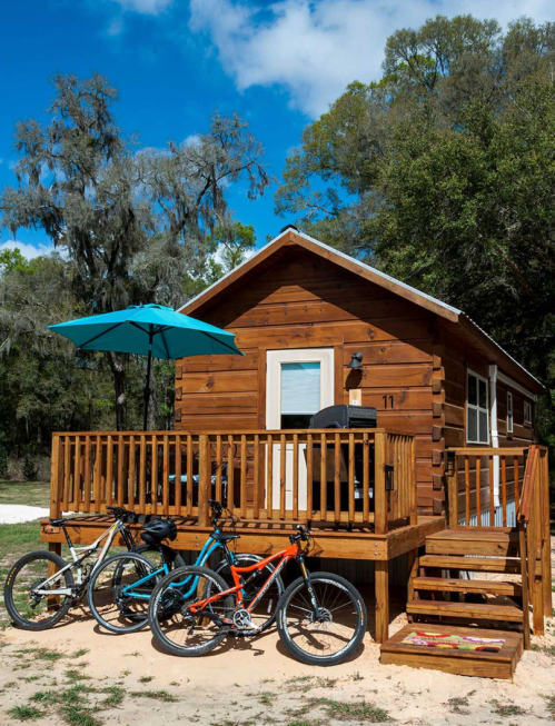 A cozy wooden cabin with a porch, surrounded by trees, featuring three bicycles parked in front.