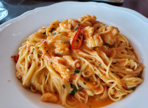 A plate of pasta with seafood, topped with a spicy red chili and garnished with herbs in a creamy sauce.