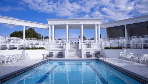 A serene outdoor pool area with white architecture, steps, and lounge chairs under a blue sky with scattered clouds.