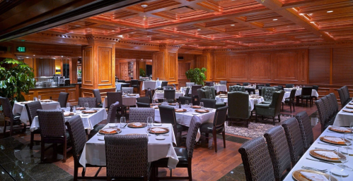 Elegant restaurant interior with wooden paneling, white tablecloths, and neatly arranged tables and chairs.