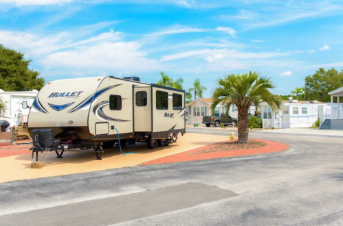 A parked RV in a sunny mobile home park, surrounded by palm trees and colorful landscaping.