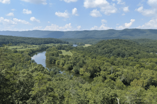 A scenic view of a river winding through lush green hills under a blue sky with fluffy clouds.