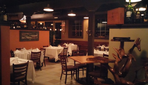 Cozy restaurant interior with white tablecloths, wooden chairs, and warm lighting, featuring a rustic decor.