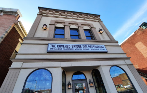 Exterior of The Covered Bridge Inn Restaurant, featuring a sign for American and Italian cuisine, with a clear blue sky.