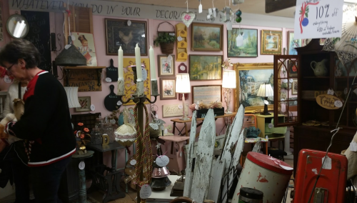 A cozy antique shop filled with vintage decor, paintings, and unique items, with a person browsing among the displays.