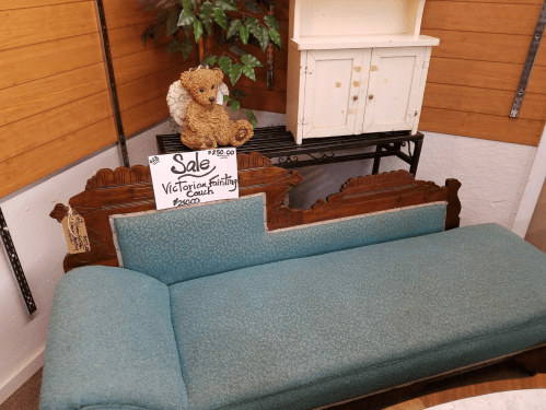 A vintage Victorian-style couch with teal upholstery, a stuffed animal on top, and a sale sign nearby.