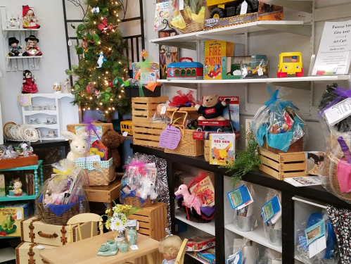 A cozy shop display filled with toys, gift baskets, and holiday decorations, including a small Christmas tree.