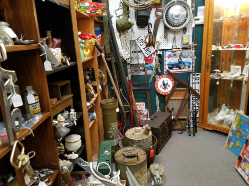A cluttered antique shop filled with various vintage items, tools, and collectibles displayed on shelves and tables.