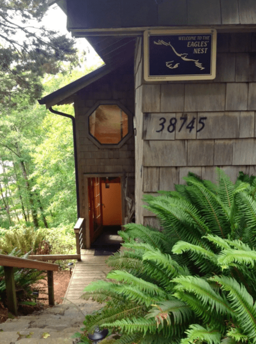 A wooden house with a sign reading "Welcome to the Eagle's Nest," surrounded by greenery and steps leading to the entrance.