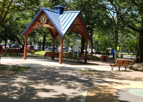 A colorful pavilion in a park with benches, surrounded by trees and pathways, inviting children to play.