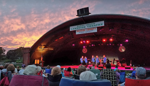A sunset over a theater stage with performers, while an audience sits in chairs enjoying the show.