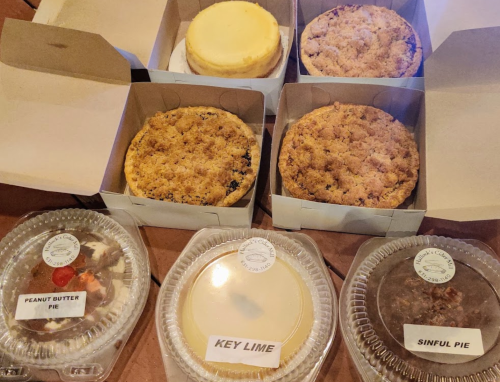 A variety of pies in boxes, including peanut butter, key lime, and a sinfully topped pie, arranged on a table.