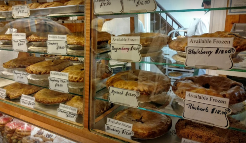 A display case filled with various frozen pies, labeled with flavors and prices, including blackberry and rhubarb.