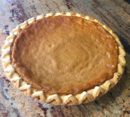 A freshly baked pie with a golden-brown filling and a decorative crust, resting on a marble countertop.