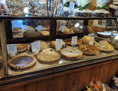 A display case filled with various pies, including pumpkin, raspberry, and apple crisp, with price tags visible.