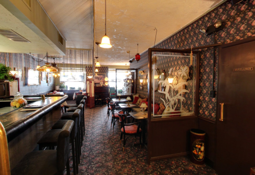 Cozy interior of a vintage bar with patterned wallpaper, wooden furniture, and warm lighting.