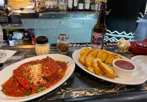 A plate of pasta in marinara sauce with cheese, alongside a plate of fried mozzarella sticks and a beer.