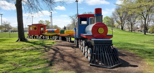 Colorful playground train structure with a locomotive and cars, set in a grassy park under a blue sky.