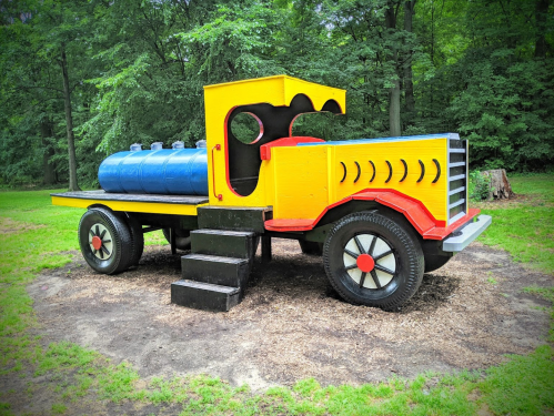 Colorful, oversized toy truck with a blue tank, set in a grassy park surrounded by trees.