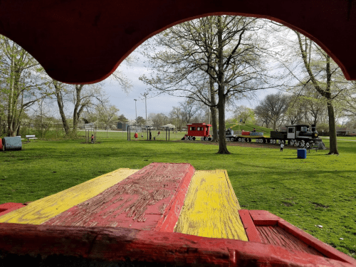 View from a colorful wooden structure overlooking a park with a train and children playing in the background.