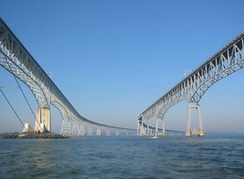 A large bridge spans over water, with clear blue skies and a calm surface below.