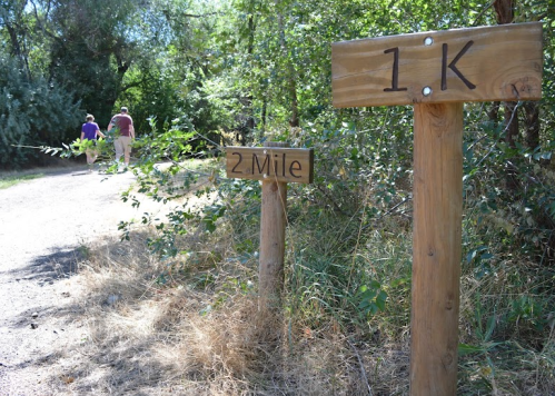 Trail signs indicating distances of 1 kilometer and 2 miles, with a path and people walking in the background.