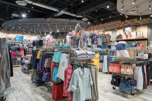 A brightly lit retail store interior filled with racks of colorful clothing and accessories for outdoor activities.
