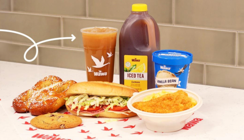 A Wawa meal featuring a sandwich, iced tea, cookies, a dessert, and mac and cheese on a table with Wawa branding.