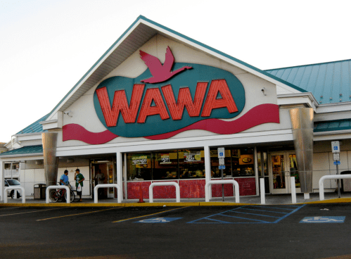 A Wawa convenience store with a colorful sign and people outside, featuring a blue roof and parking area.