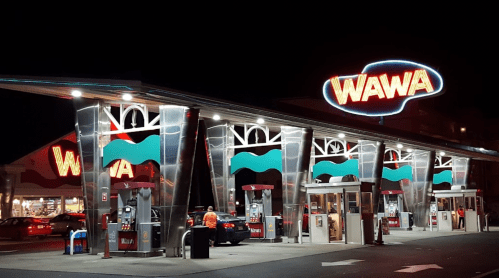 A brightly lit Wawa convenience store at night, featuring gas pumps and a large illuminated sign.