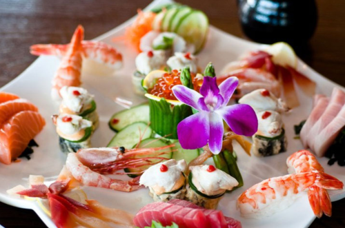 A beautifully arranged sushi platter featuring various sushi, sashimi, and a purple flower garnish.