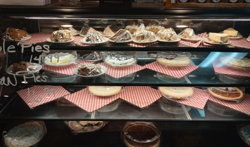 A display case filled with various pies on red checkered paper, showcasing different flavors and styles.