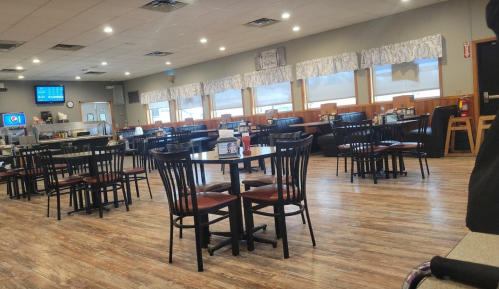 A spacious, empty restaurant with wooden floors, black chairs, and large windows letting in natural light.