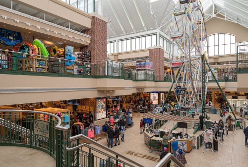 A spacious indoor shopping area featuring a ferris wheel, stores, and shoppers exploring the vibrant space.